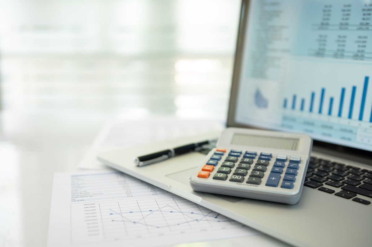 Calculator, account statement and financial reports beside a laptop